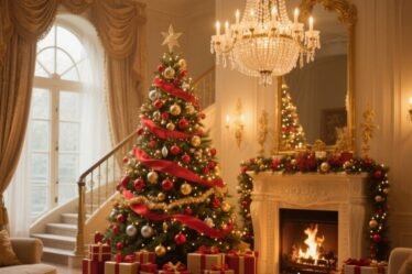 Luxurious artificial Christmas tree decorated in red and gold ornaments beside a fireplace, chandelier above, glowing lights, and wrapped presents below.